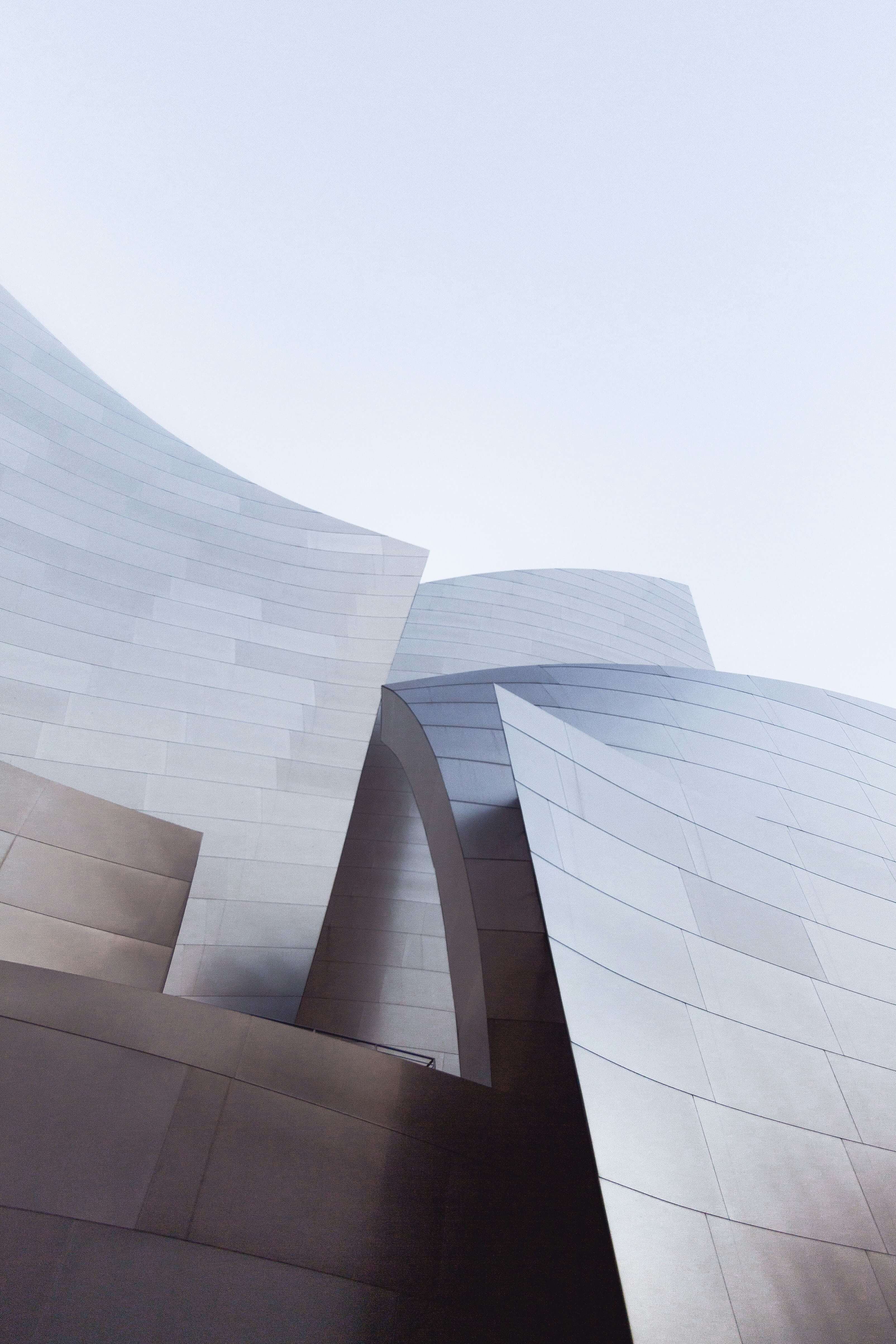 Contemporary architecture with overlapping curved metallic surfaces in soft light, embodying the smooth and innovative strategies of Caldera Capital.